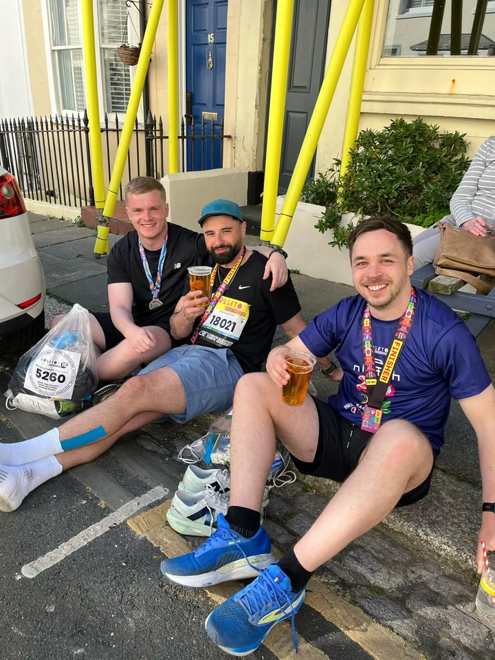 Three runners relaxing with drinks and finisher medals after a race.